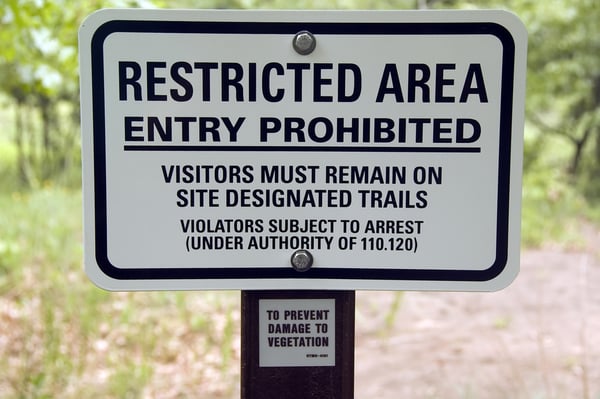 Warning sign by trail in state park RESTRICTED AREA . . . VIOLATORS SUBJECT TO ARREST . . .